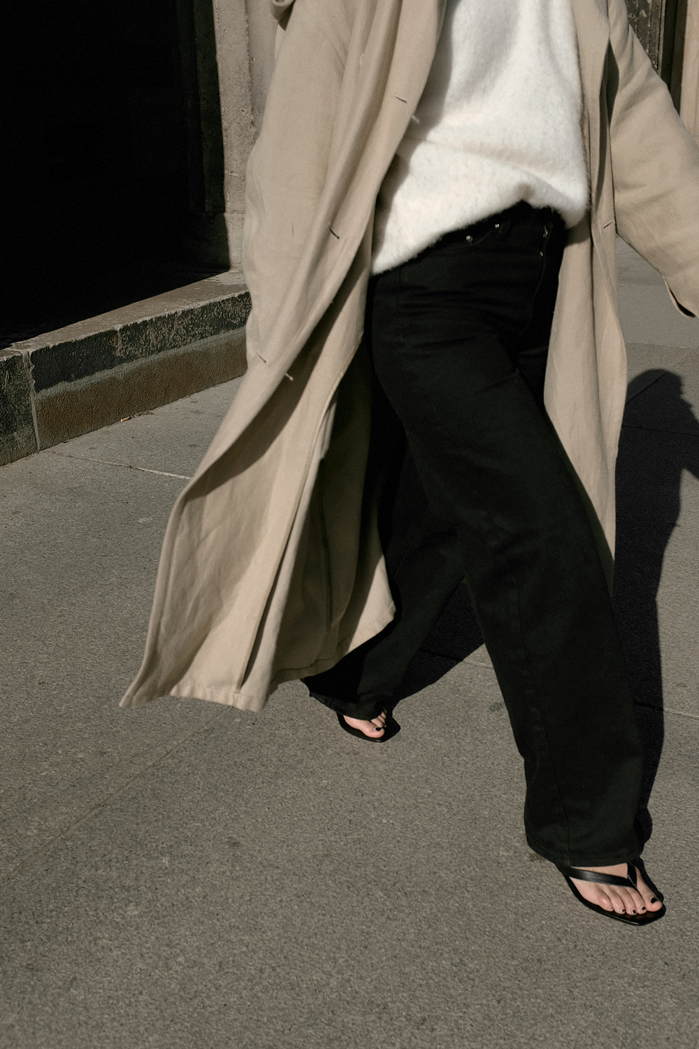 Nisi is wearing: Black wide leg denim jeans – Edited the label, White alpaca-blend sweater – Filippa K, Trenchcoat – & Other Stories, Baby Boss bag – Little Liffner, Heeled flip-flops – Totême, Tire earrings – All Blues