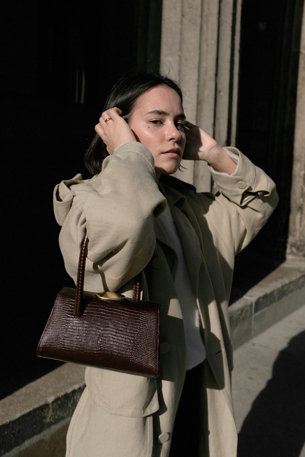 Nisi is wearing: Black wide leg denim jeans – Edited the label, White alpaca-blend sweater – Filippa K, Trenchcoat – & Other Stories, Baby Boss bag – Little Liffner, Heeled flip-flops – Totême, Tire earrings – All Blues