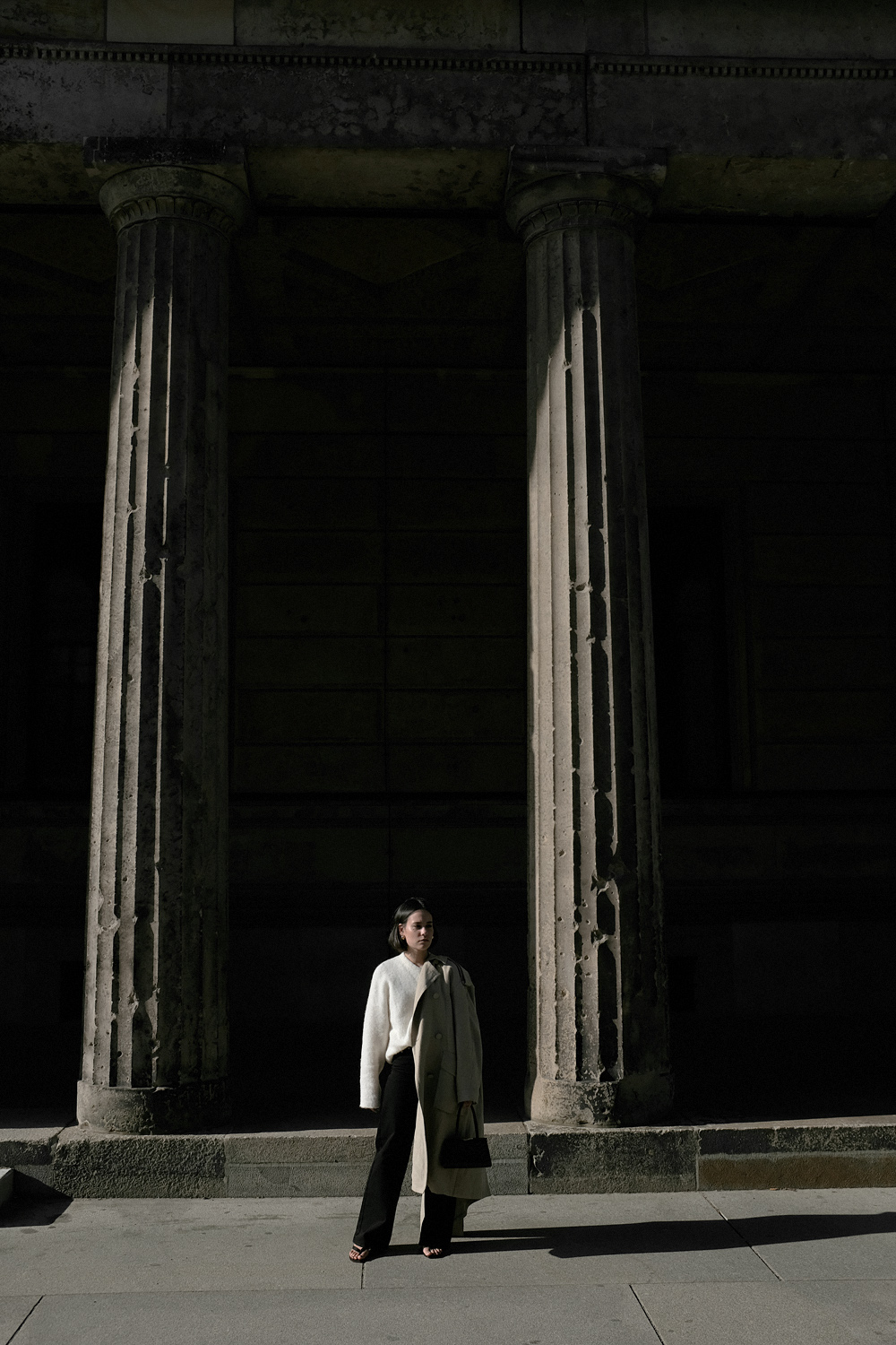 Nisi is wearing: Black wide leg denim jeans – Edited the label, White alpaca-blend sweater – Filippa K, Trenchcoat – & Other Stories, Baby Boss bag – Little Liffner, Heeled flip-flops – Totême, Tire earrings – All Blues