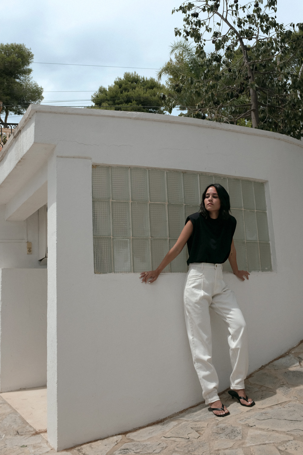 Nisi is wearing: Padded muscle shirt EDITED THE LABEL, White denim jeans EDITED THE LABEL, Flip flop heels TOTÊME, Fat Snake ring in silver ALL BLUES, Fat gold ring DAPHINE