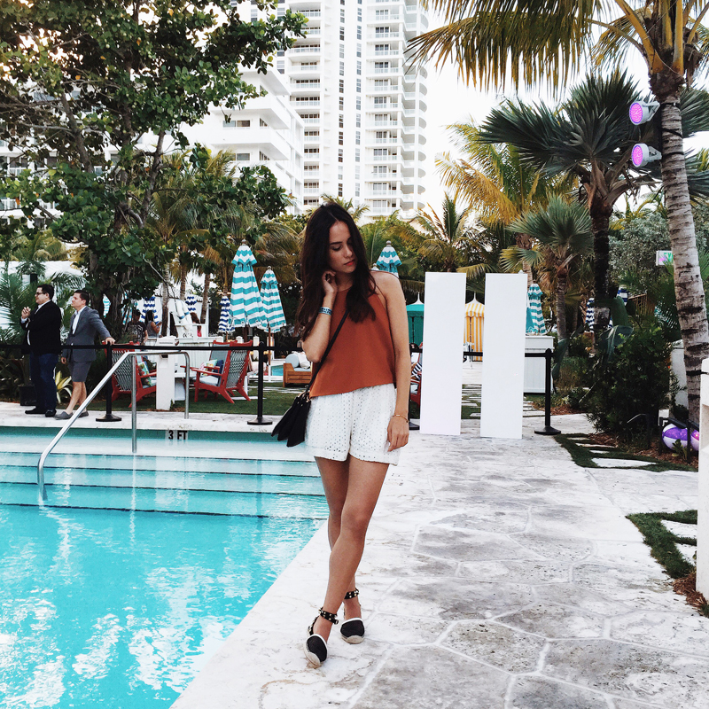 Nisi is wearing a brick red crop top, white lace shorts, Rebecca Minkoff espadrilles and a Céline Trio Bag at Urban Decay Summer Nights party in Miami