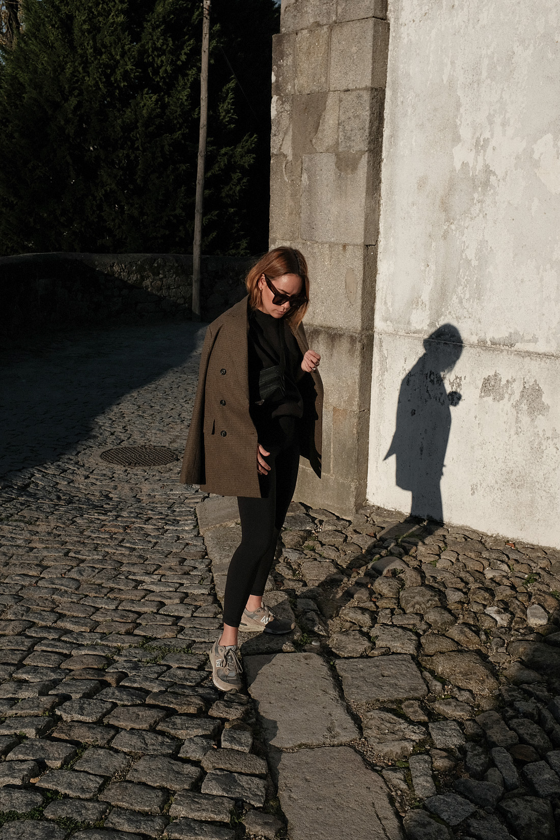 Desi is wearing an oversized blazer, Fruit of the Loom jumper, Lululemon leggings, New Balance 991 sneakers, Céline Tilda sunglasses Prada belt bag in Porto