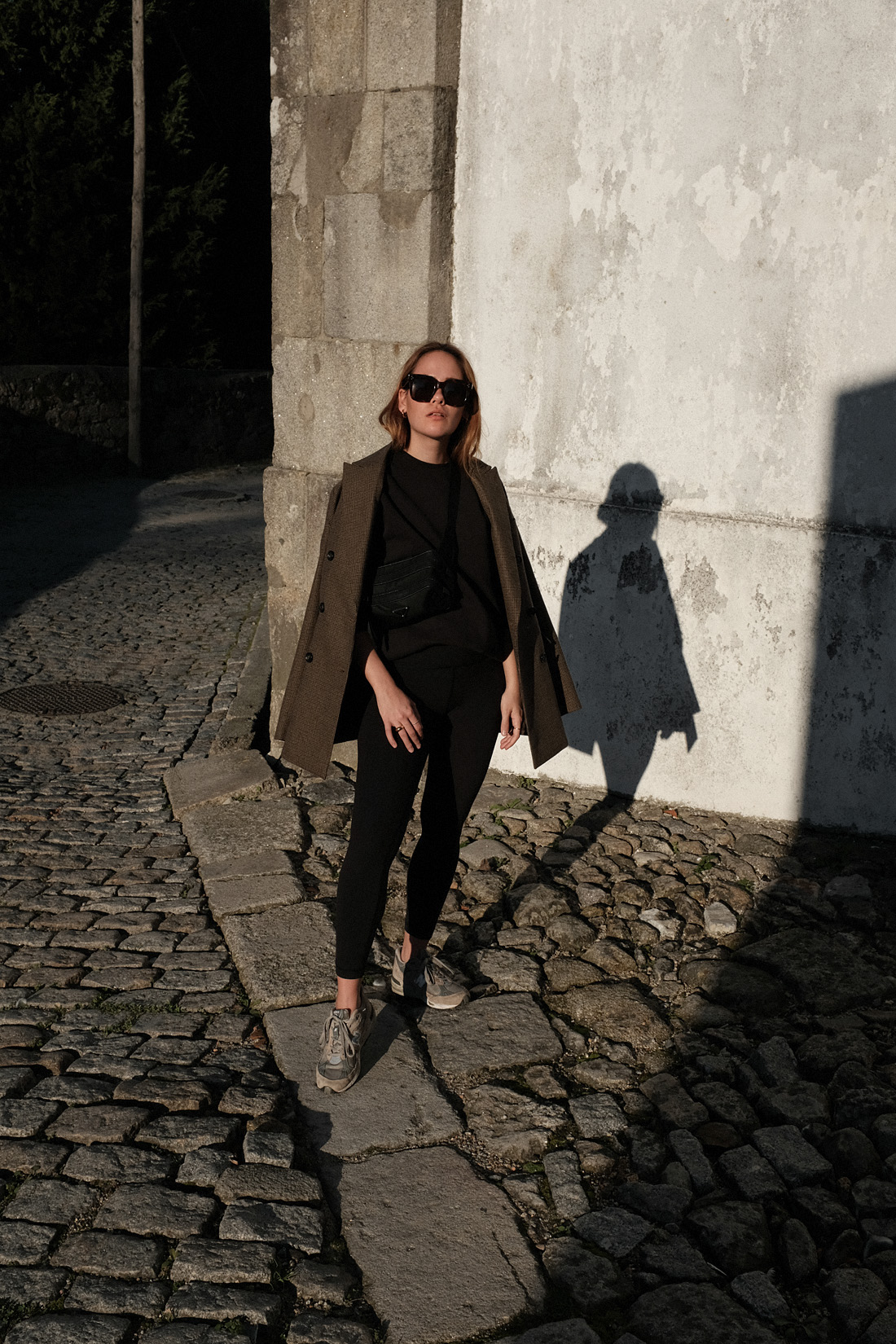 Desi is wearing an oversized blazer, Fruit of the Loom jumper, Lululemon leggings, New Balance 991 sneakers, Céline Tilda sunglasses Prada belt bag in Porto