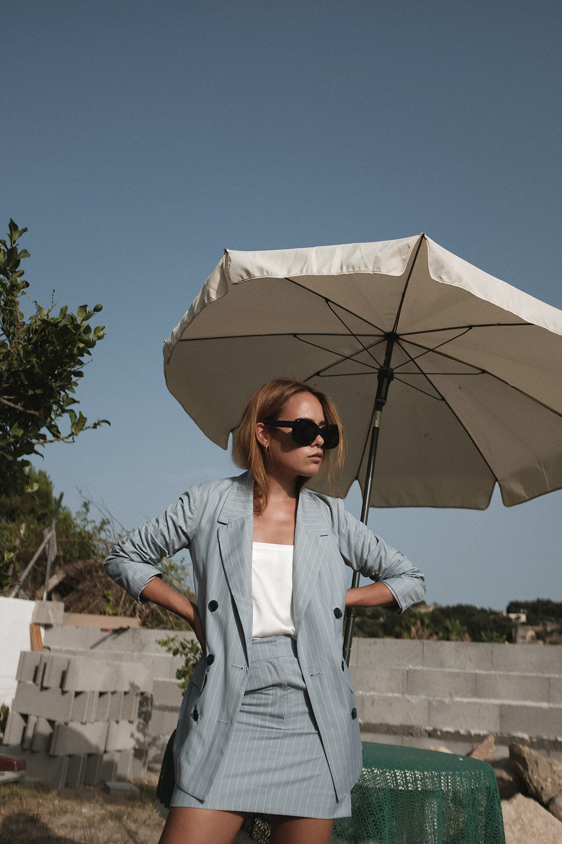 Desi is wearing: The Row Bow mules, Céline Sunglasses, Edited the Label Pinstripe blazer and pinstripe pencil skirt, Edited the Label silky white camisole