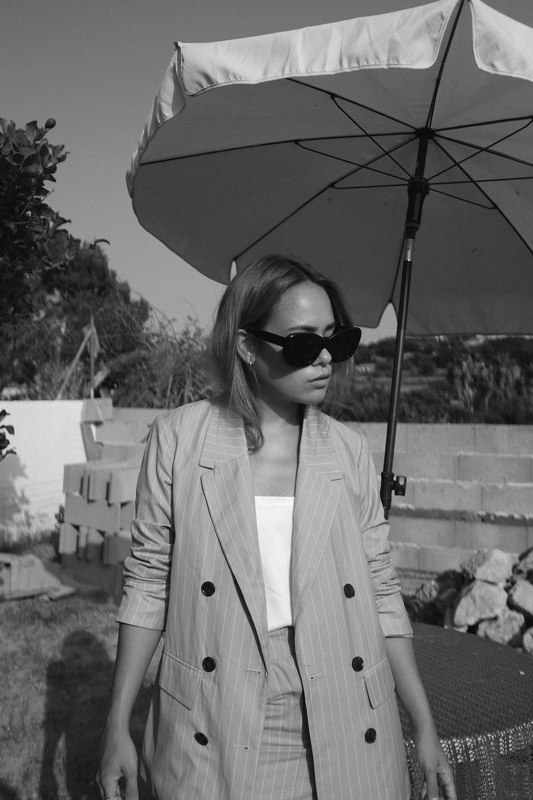 Desi is wearing: The Row Bow mules, Céline Sunglasses, Edited the Label Pinstripe blazer and pinstripe pencil skirt, Edited the Label silky white camisole