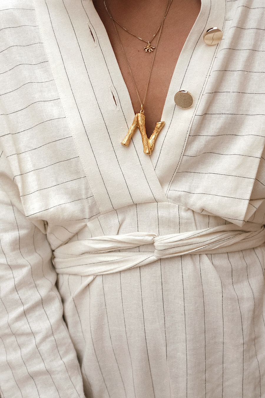 Nisi is wearing: The Row Ascot bag,  Céline Alphabet necklace, Striped dress, Black strappy sandals, Coral necklace, Gold pearl earring