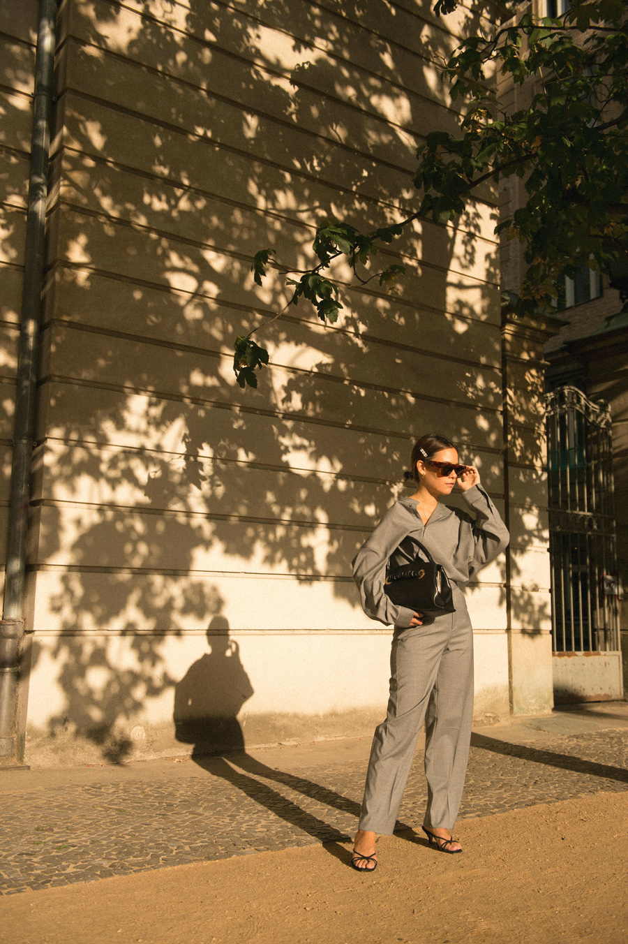 Nisi is wearing: Totême Grey shirt and trousers, Céline Purse with Eyelets bag, Strappy sandals, Céline Sunglasses, Pearl hair clip