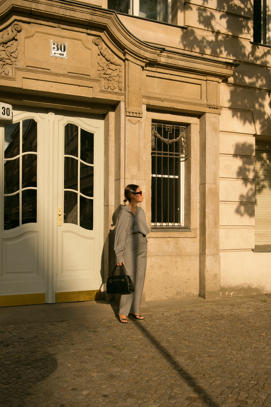 Nisi is wearing: Totême Grey shirt and trousers, Céline Purse with Eyelets bag, Strappy sandals, Céline Sunglasses, Pearl hair clip